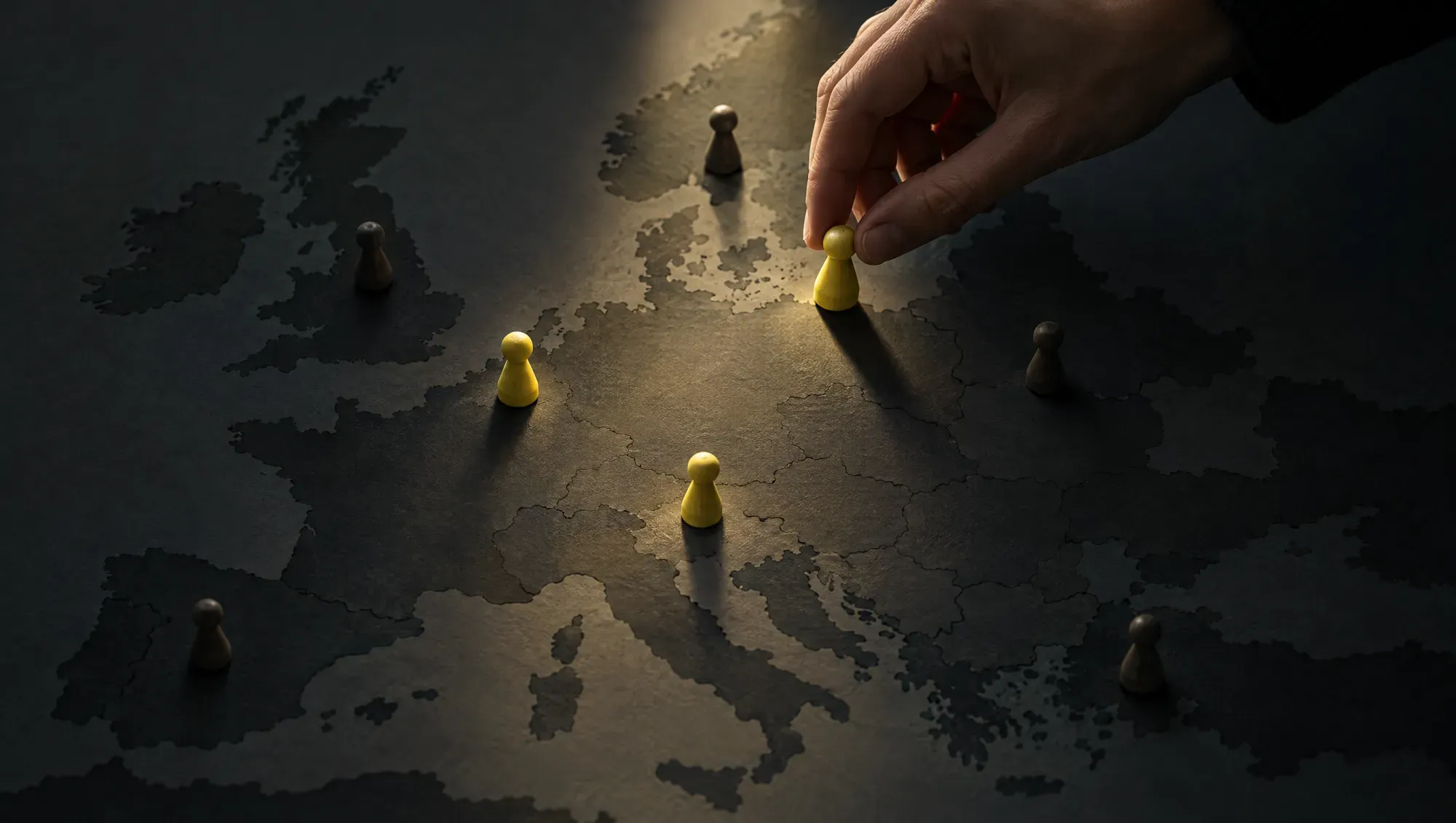 Una mappa scura dell'Europa con pochi segnaposto: tre sono gialli e una mano ne sta posizionando uno
