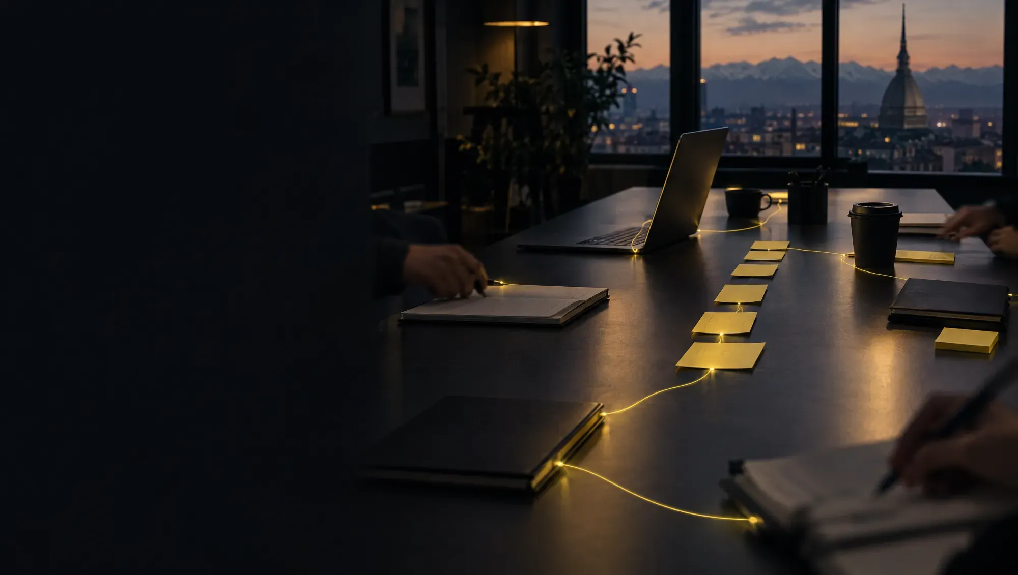 Une table de travail au coucher du soleil dans un bureau de Turin, avec des carnets, un ordinateur portable et des notes alignées, reliés par de fins fils de lumière jaune