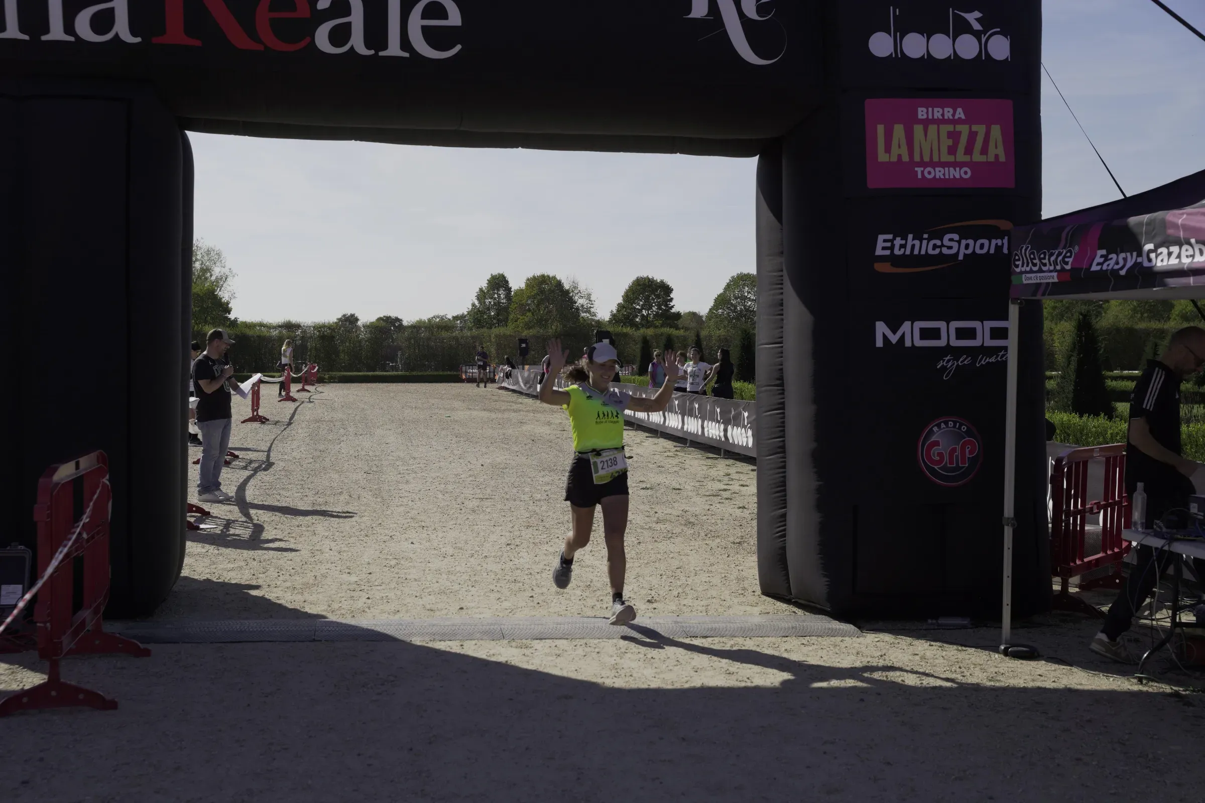 Una runner taglia il traguardo della Maratona Reale salutando con le mani alzate, sotto l'arco con gli sponsor