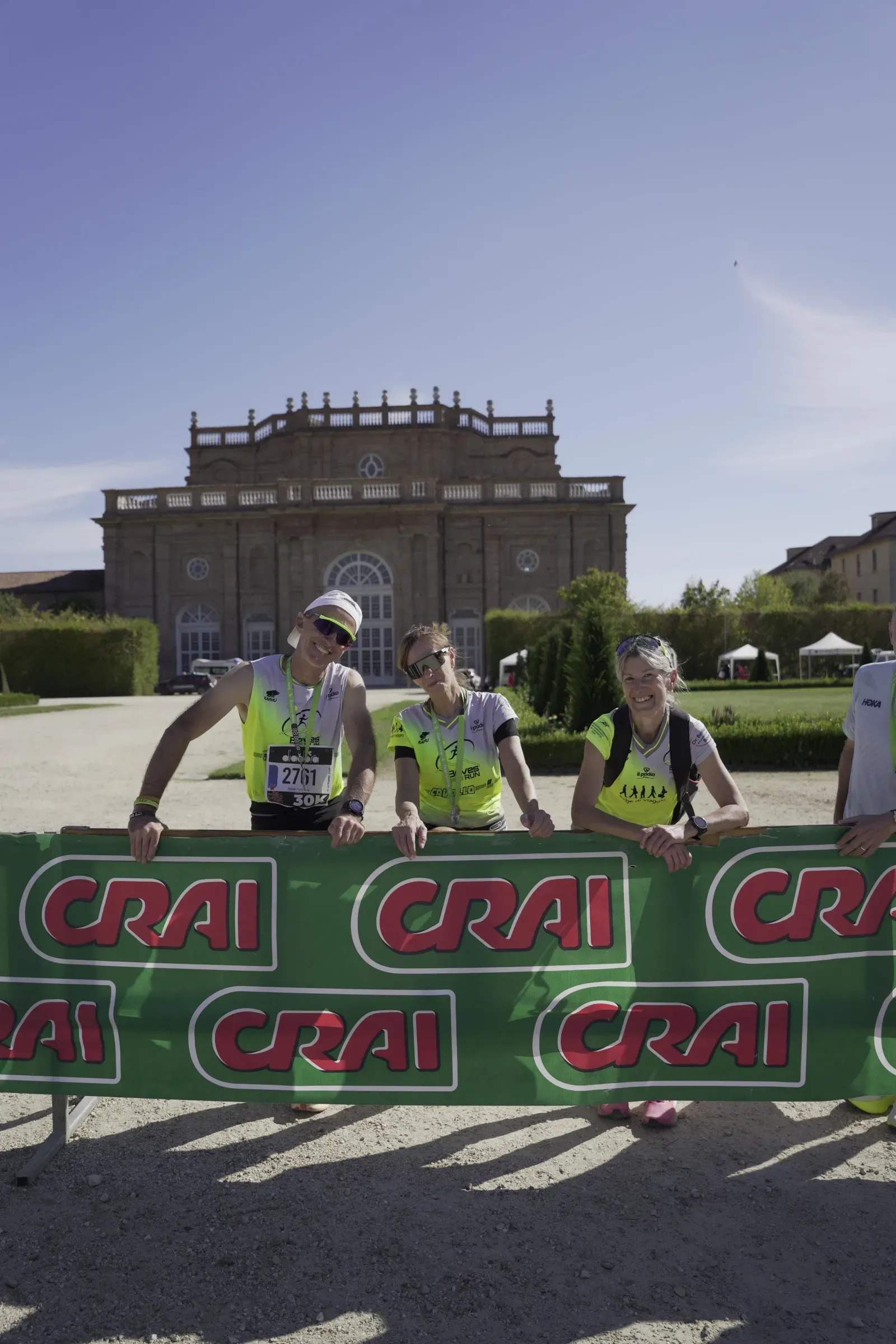 Tre runner con la medaglia appoggiati alle transenne CRAI, con la Citroniera della Reggia di Venaria alle spalle