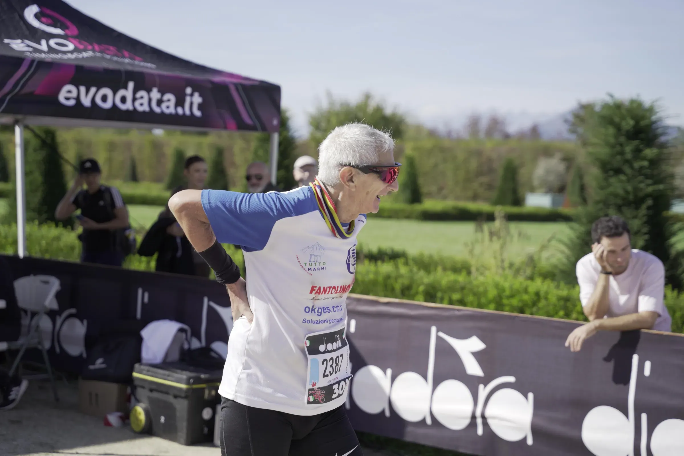 Un runner con i capelli bianchi e la medaglia al collo, dopo la 30 km di Una Corsa da Re, si tiene la schiena e ride