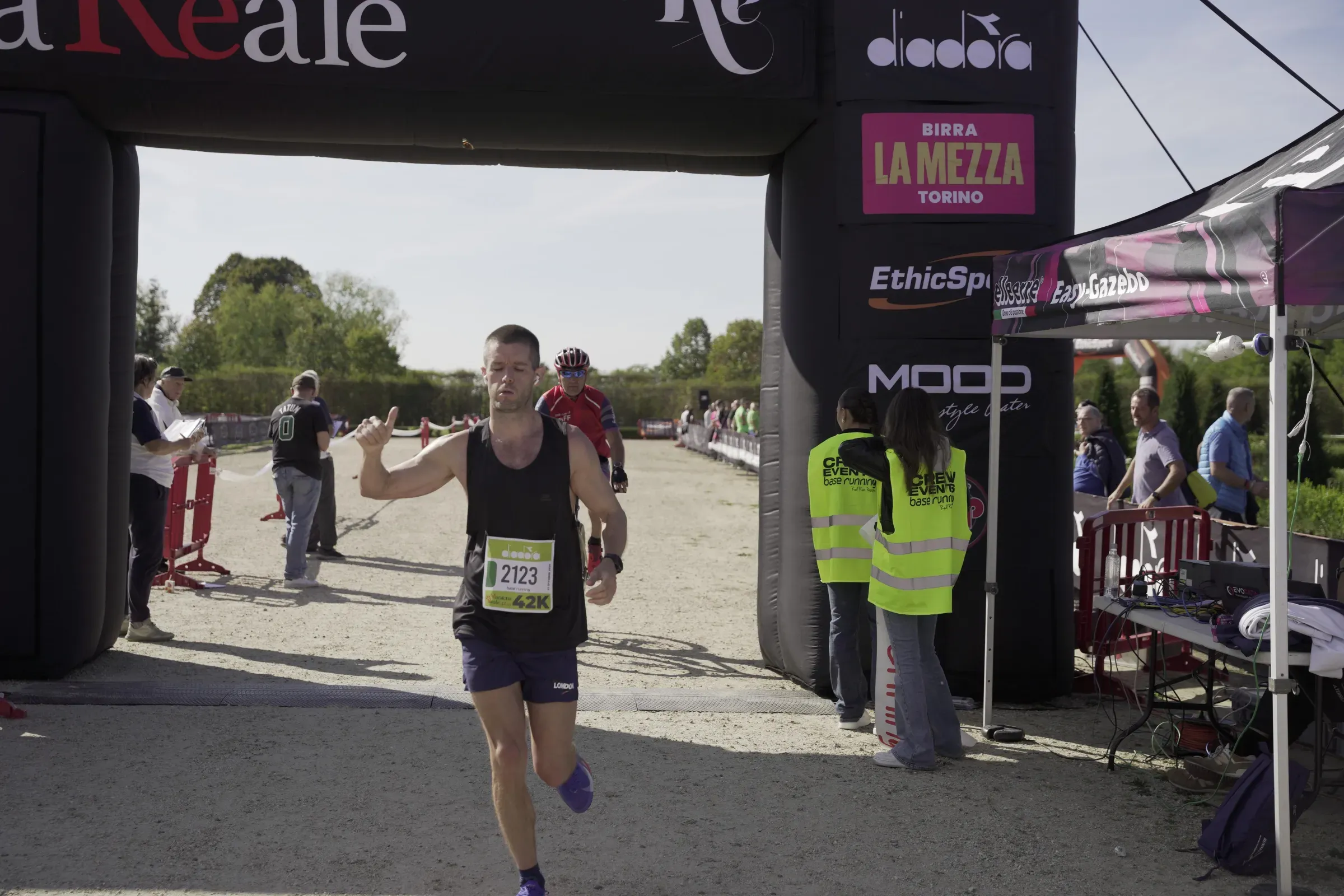 Un maratoneta alza il pollice all'arrivo, accanto ai volontari della crew Base Running