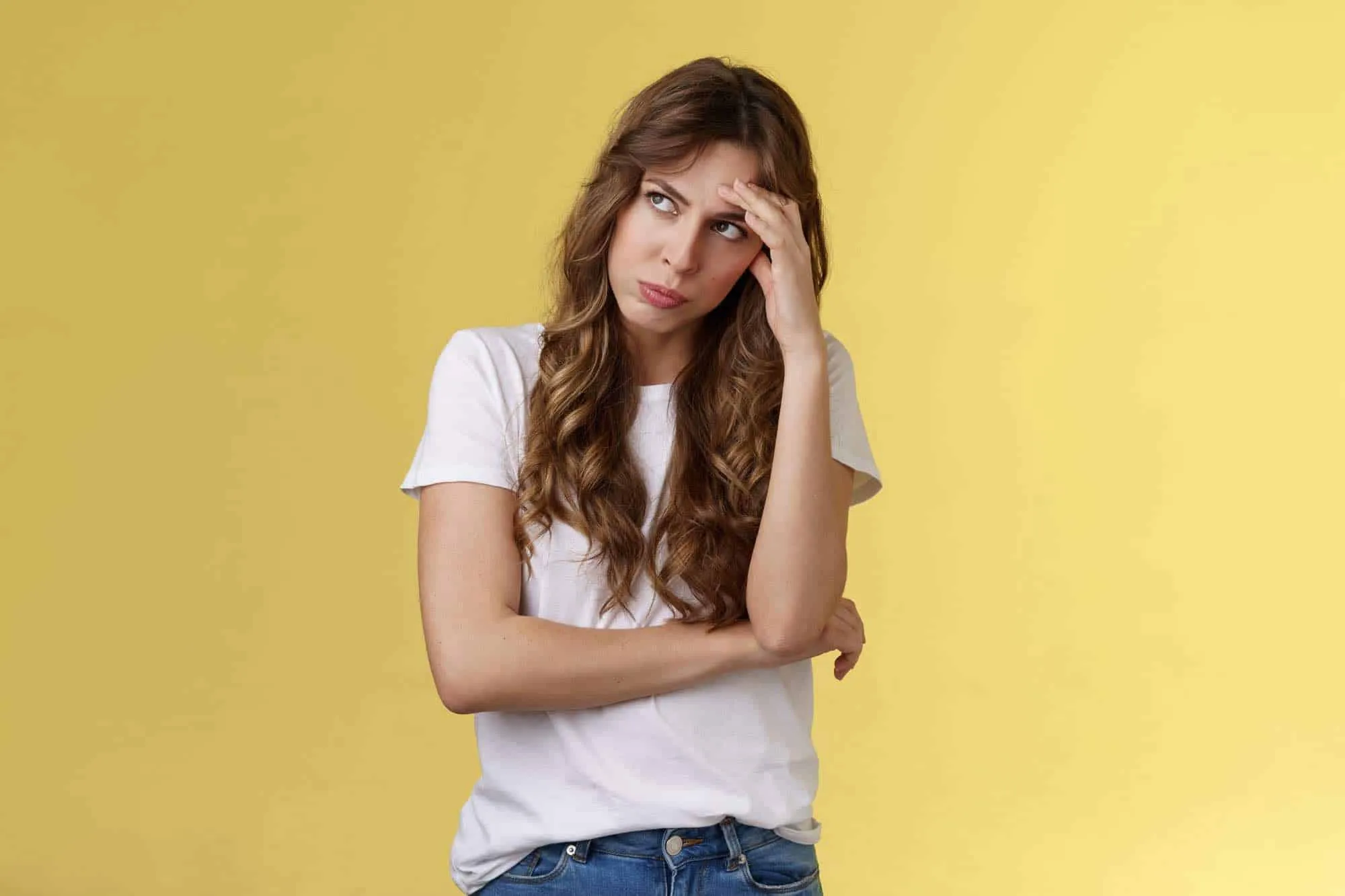 Ragazza con i capelli ricci e maglietta bianca, mano sulla fronte e sguardo perplesso, su sfondo giallo