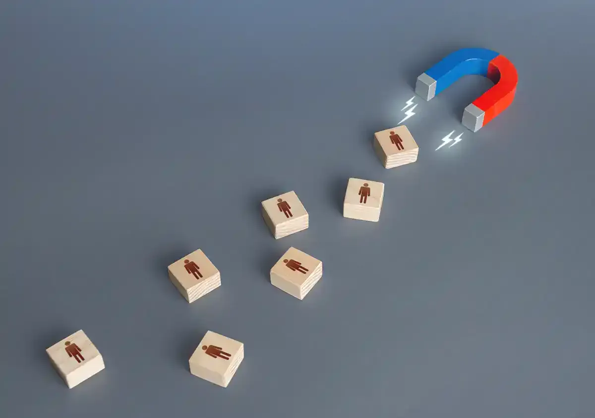 Aimant rouge et bleu qui attire une rangée de petits cubes en bois portant des silhouettes de personnes, sur fond gris