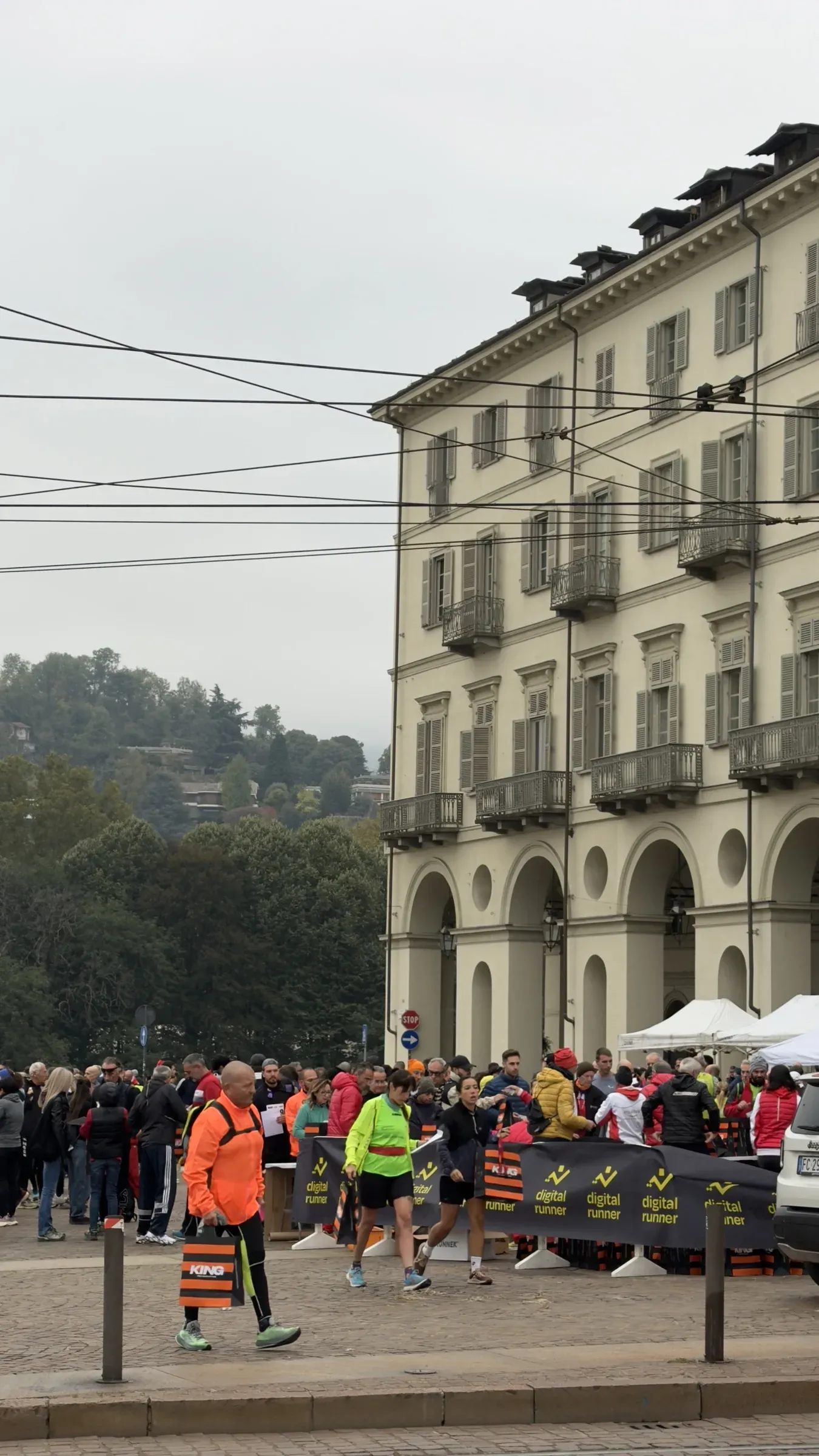 Runner in piazza Vittorio Veneto a Torino al ritiro dei pacchi gara della Mezza e della Dieci che Vale, con le transenne Digital Runner e la collina sullo sfondo