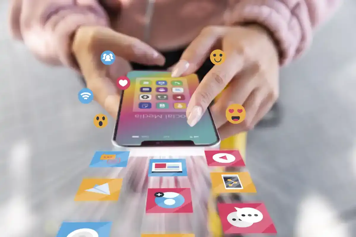 Hands touching a smartphone from which app icons, emojis and social media notifications are emerging