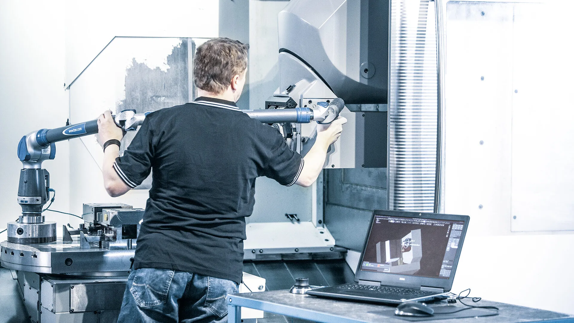 Tecnico al lavoro su una macchina di misura con il portatile aperto