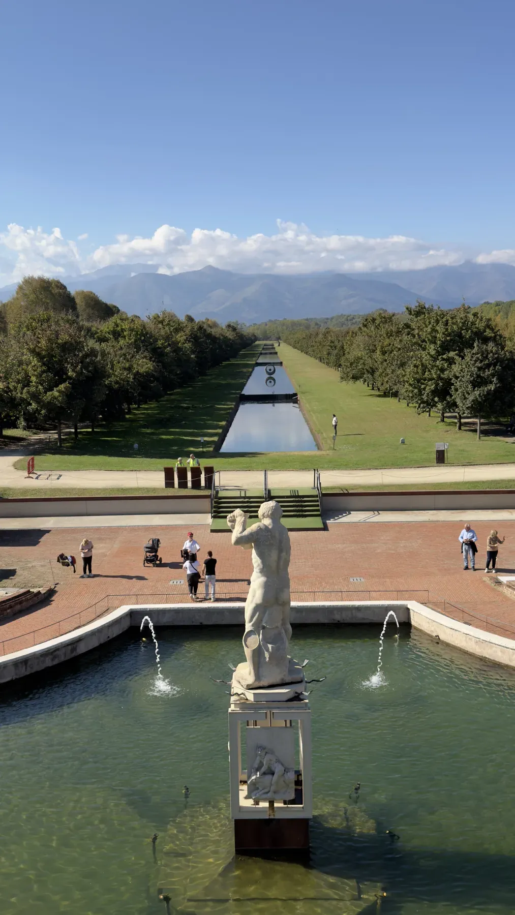 La Fontana d'Ercole vista dalla Reggia di Venaria, con il canale dei Giardini, il viale alberato e le Alpi sotto il cielo azzurro